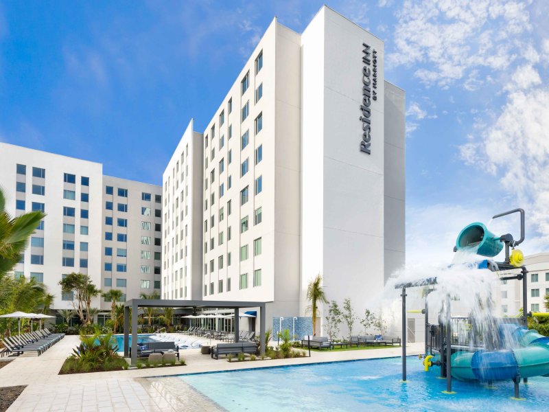 Photo showing a swimming pool with water fountain play area, with a tall white hotel building in the background. Residence Inn by Marriott San Juan Isla Verde.