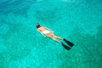 Woman snorkeling in white bathing suit against turquoise waters. 