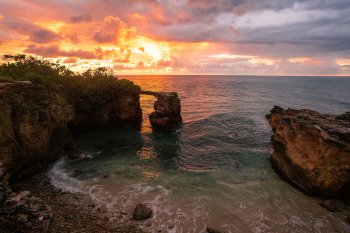 A dramatic sunset over the ocean with a beach surrounded by rock formations in the foreground