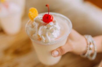 A woman holds a cup of a frozen piña colada with a cherry on top.