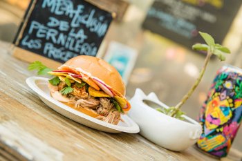 Un sándwich con muchos aderezos y una colorida lata de cerveza se muestran en una mesa en Lote 23, un parque de camiones de comida en el barrio de Santurce de San Juan, Puerto Rico.