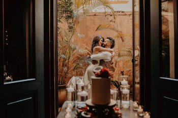 Una pareja se abraza en un balcón con un pastel de bodas en primer plano en El Convento en San Juan, Puerto Rico.