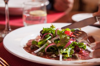 A person cutting a plate of salad greens on top of thinly sliced beef at Restaurante Alexandra.