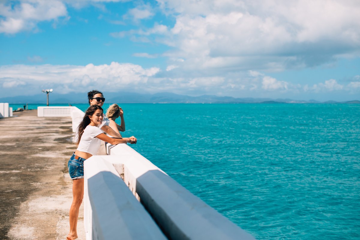 A small group stands along the side of the pier looking out at the bright blue water