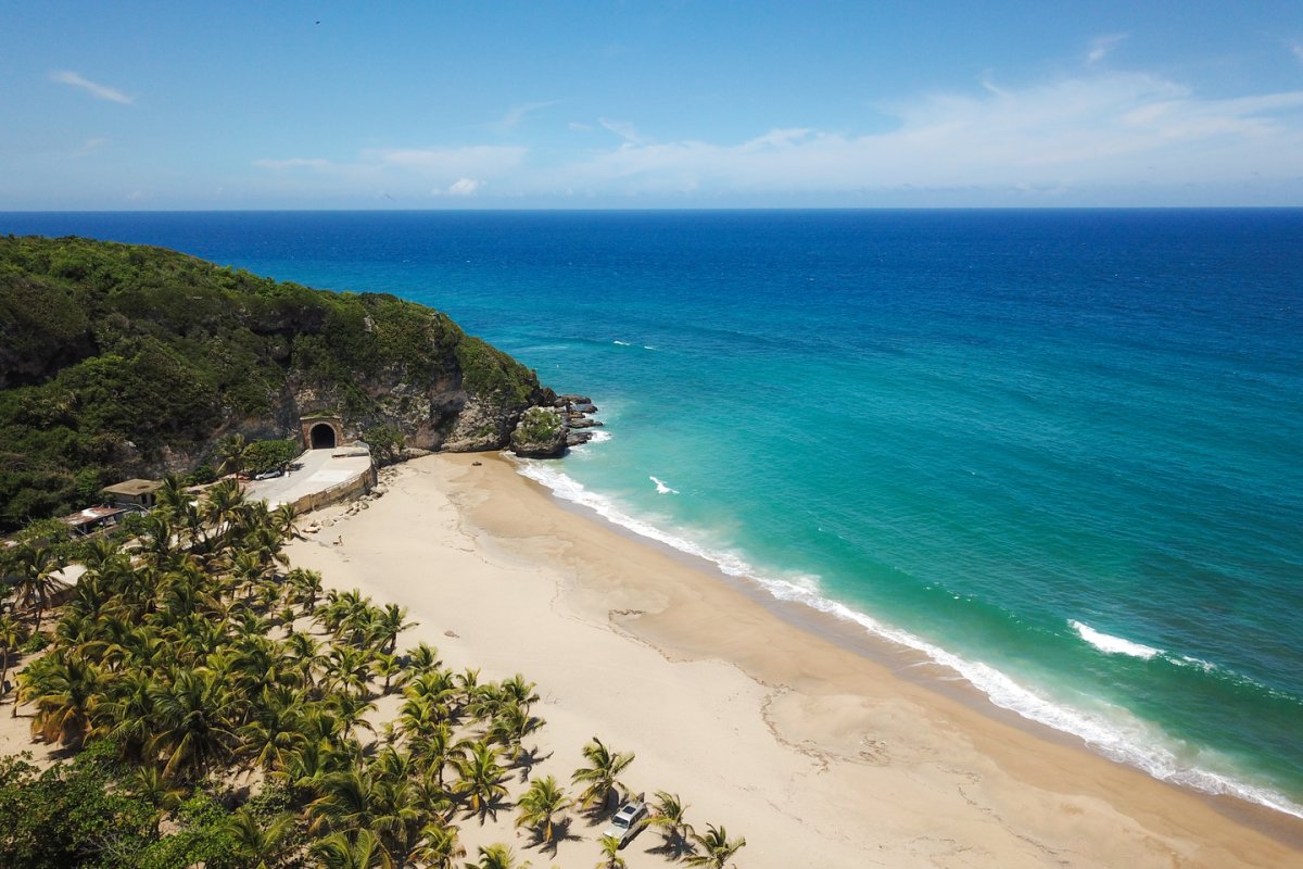 Una vista aérea del Túnel de Guajataca adyacente a una playa de arena blanca y mar turquesa.