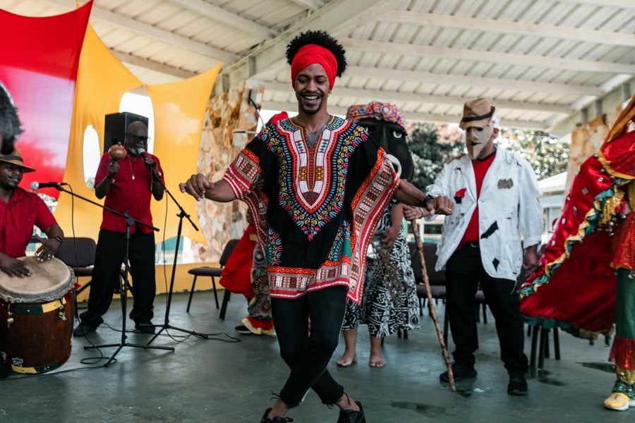 Afro-Caribbean man dances to the tune of bomba music, while other dancers and musicians are in the background. 