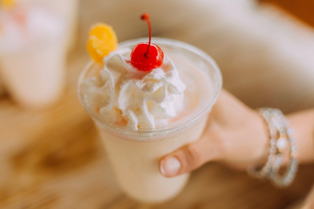 A woman holds a cup of a frozen piña colada with a cherry on top.