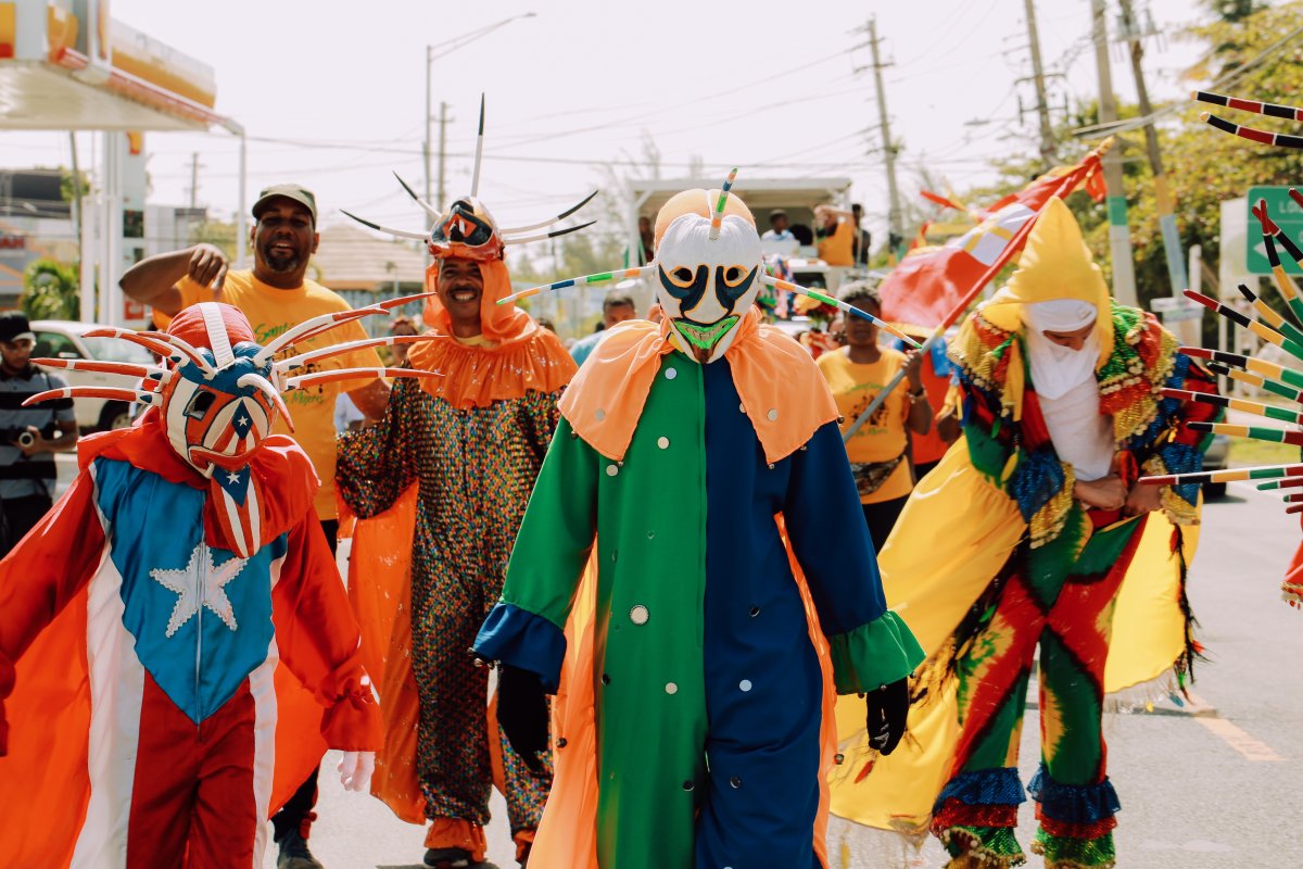 A colorful group of people dressed in the tradional attire of Puerto Rican vejigantes, which includes colorful masks. 