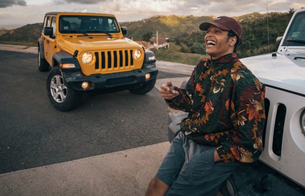 A smiling guy leans against the front of a car