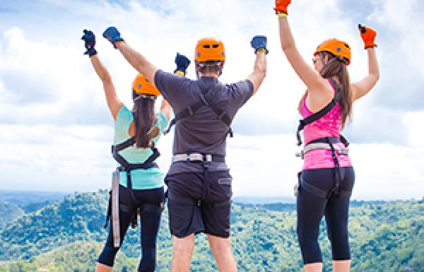 Three people with hands in the air wearing zipline gear.