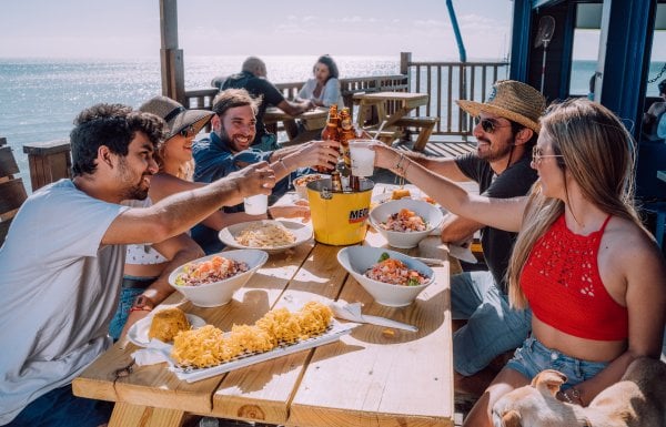 A group of friends toasts at an outdoor table overlooking the sea.