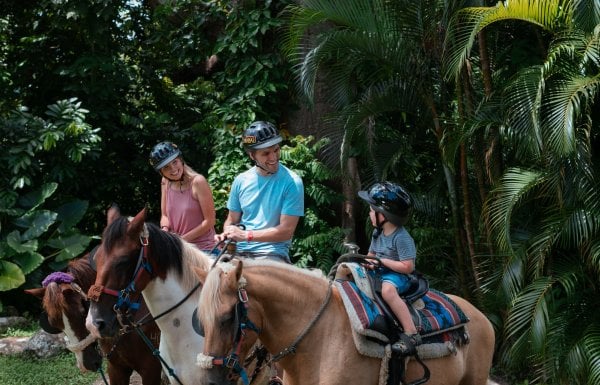 A famiy of three sitting atop three horses in a green outdoor space.