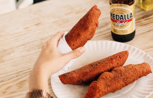 Person holds a Puerto Rican fritters known as alcapurria with a local beer in the background.