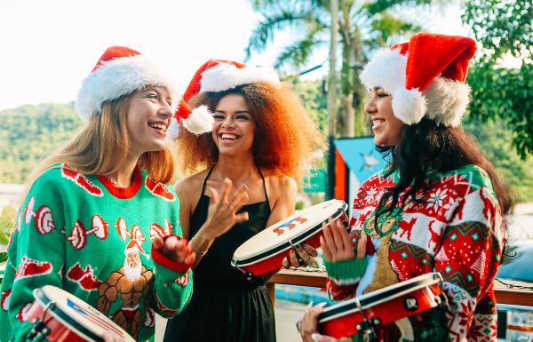 Tres jóvenes con gorros de Papá Noel y suéteres coloridos y acogedores tocan a los panderos en Puerto Rico.