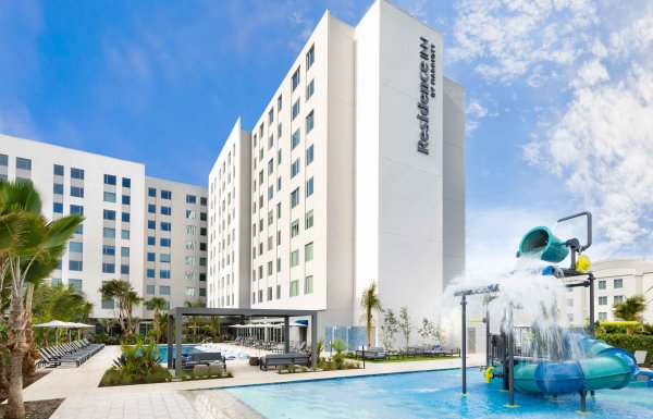 Photo showing a swimming pool with water fountain play area, with a tall white hotel building in the background. Residence Inn by Marriott San Juan Isla Verde.