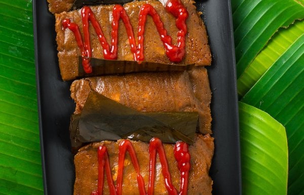 Plate of pasteles with and without ketchup on top of banana leaves.