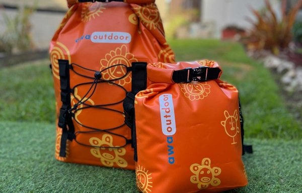 Two dry bags in the bright orange shade of Puerto Rico Sunshine sit on display atop green grass.