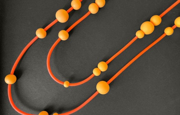 Overhead shot of a beaded necklace by Knot Predictable in shades of orange on a black background.