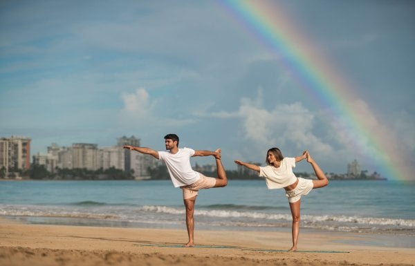 Una pareja practica yoga en una playa con un arco iris sobre sus cabezas en el hotel Fairmont El San Juan.