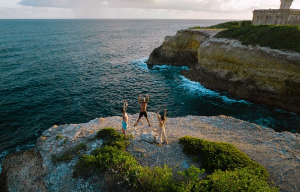 Three people practice yoga on an oceanside cliff during a retreat at Finca Victoria. Vieques, Puerto Rico.