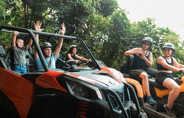 Man and son celebrating with their hands up inside an ATV going through the rainforest in Puerto Rico. The mother in another ATV and two other women on ATVs surround them.