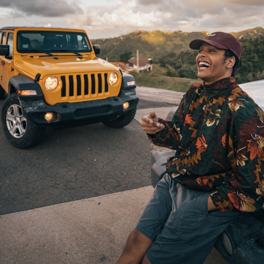 A smiling guy leans against the front of a car