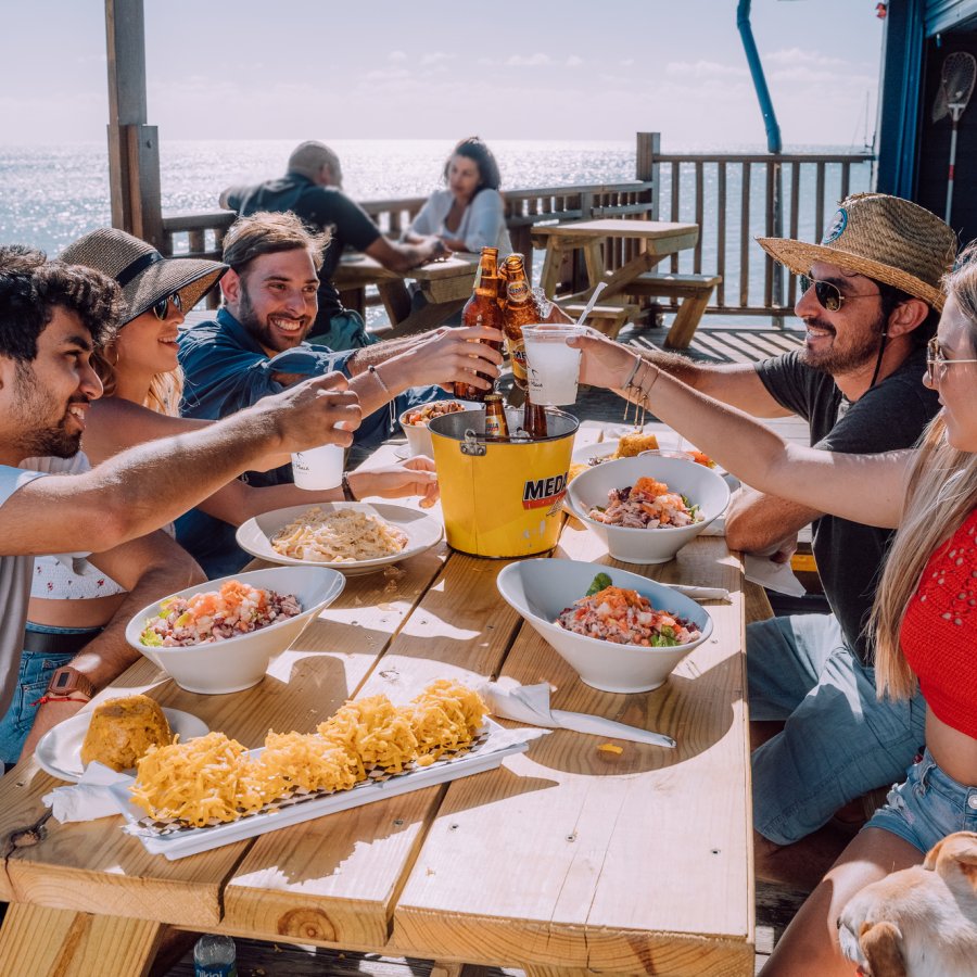 A group of friends toasts at an outdoor table overlooking the sea.