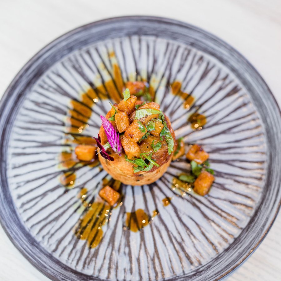 Overhead shot of a creatively plated dish by Chef Mario Pagan on a blue-and-white striped plate.