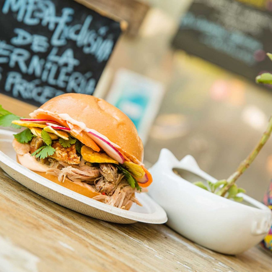 Un sándwich con muchos aderezos y una colorida lata de cerveza se muestran en una mesa en Lote 23, un parque de camiones de comida en el barrio de Santurce de San Juan, Puerto Rico.