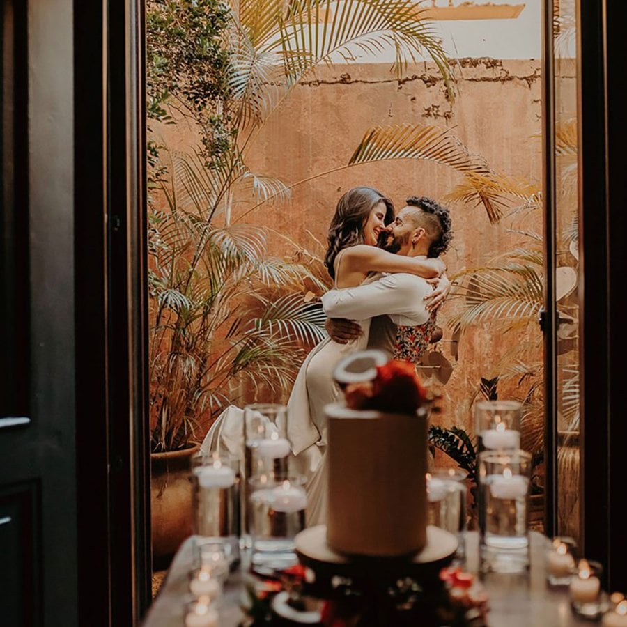 Una pareja se abraza en un balcón con un pastel de bodas en primer plano en El Convento en San Juan, Puerto Rico.