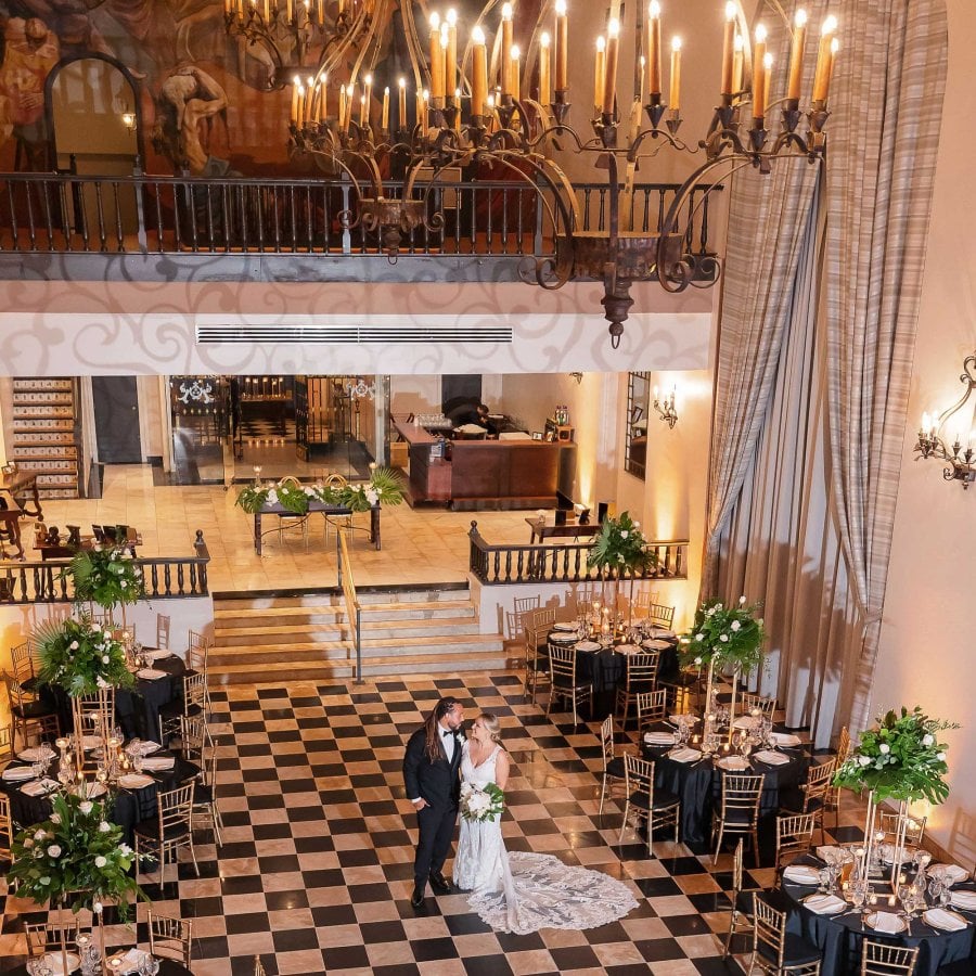 Una novia y un novio aparecen fotografiados desde arriba en los azulejos a cuadros blancos y negros del Hotel El Convento en San Juan, Puerto Rico.