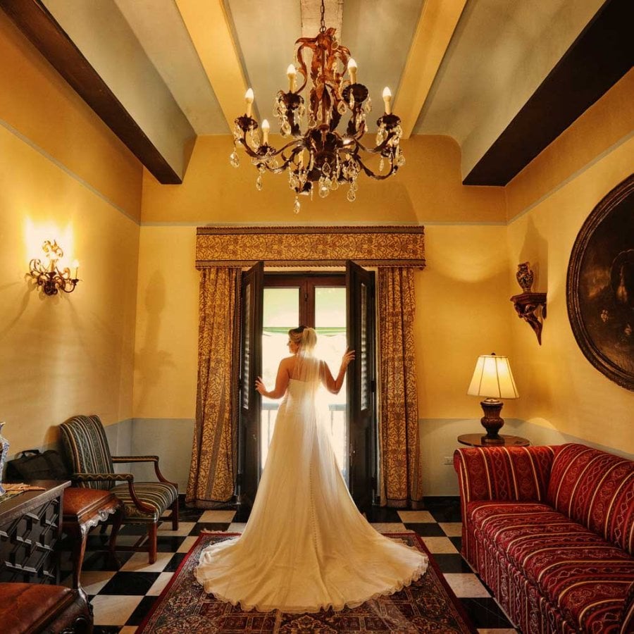 Una novia, fotografiada desde atrás, abre una gran ventana histórica en el Hotel El Convento en el Viejo San Juan, Puerto Rico. Foto de Noel Pilar.