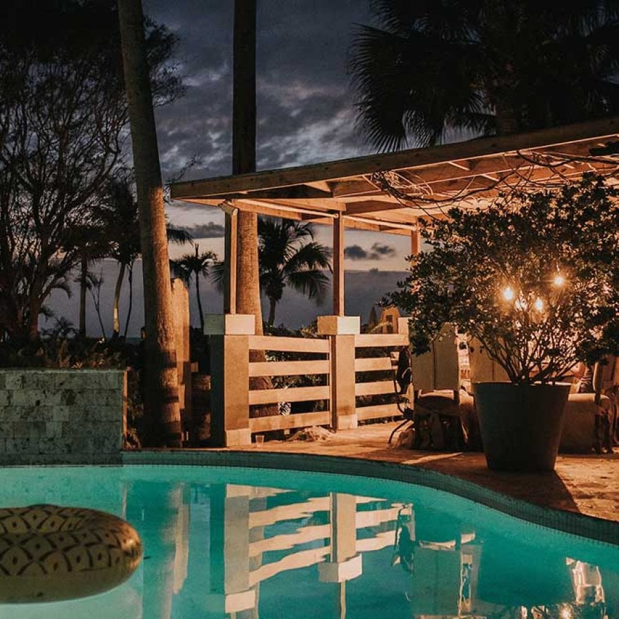 Un patio con vistas a una piscina en un entorno tropical se ilumina por la noche. Villa Montaña Beach Resort, Aguadilla, Puerto Rico.