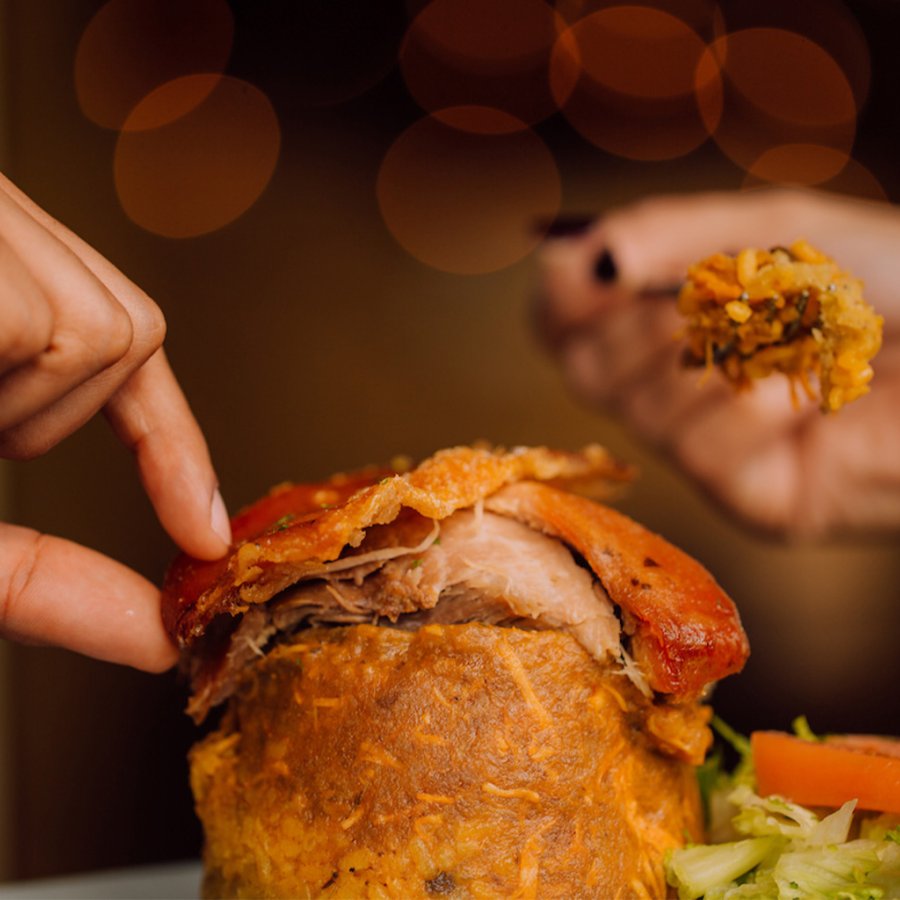 Two hands picking at a plate of mofongo, pilled high with red meat.