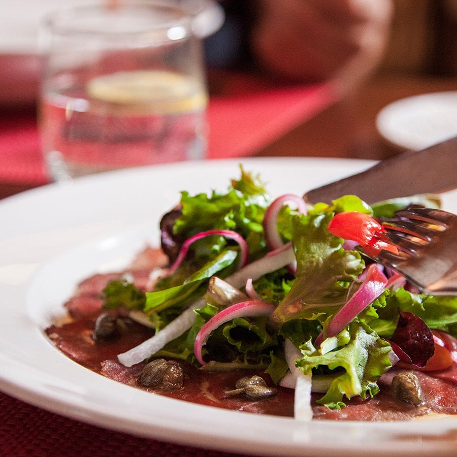 A person cutting a plate of salad greens on top of thinly sliced beef at Restaurante Alexandra.