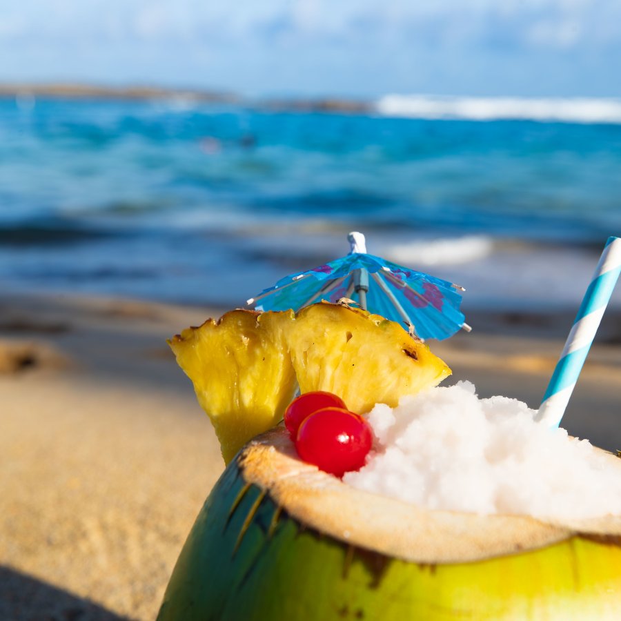 Foto de coco relleno de piña colada con una playa de fondo.