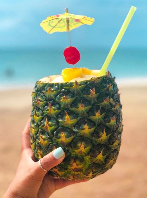 A hand holding a pineapple filled with piña colada.